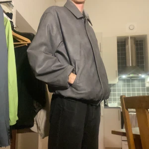 Grå oversized skinnjacka - Säljer en grå oversized skinnjacka med klassisk krage och dragkedja framtill. Jackan har en clean look med raka linjer och två sidofickor. Perfekt för dig som gillar en enkel men stilren vibe. Passformen är loose och ärmarna är långa.