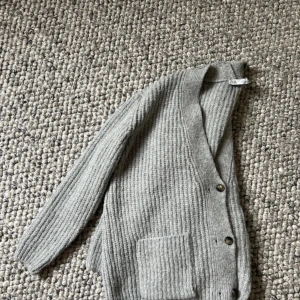 Grå stickad kofta från Zara - Mysig grå stickad kofta från Zara med djup v-ringning, stora framfickor och knappar framtill. Perfekt för lager-på-lager och chill dagar. Tjock ribbstickad struktur som ger en avslappnad vibe.