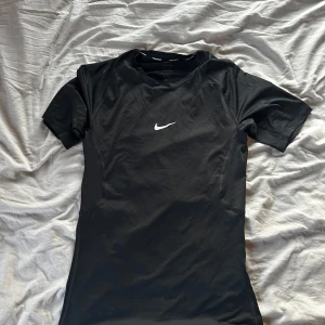 Nike Pro svart tight träningströja - Svart Nike Pro t-shirt med vit logga på bröstet. Tight fit och tillverkad i Dri-FIT-material som andas, perfekt för intensiva träningspass. Kortärmad modell med sportig look och bekväm passform.