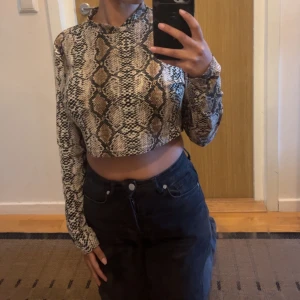 Croppad långärmad topp med ormmönster - Säljer en croppad långärmad topp med coolt ormmönster i beige, brunt och svart. Toppen har hög hals och är figurnära, perfekt för dig som vill sticka ut. Materialet känns stretchigt och mjukt mot huden.