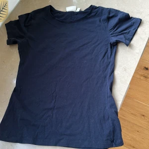 Mörkblå t-shirt från Kappahl - En basic mörkblå t-shirt från Kappahl i storlek S. T-shirten har rund halsringning och korta ärmar, perfekt för en clean och enkel stil. Tillverkad i mjuk bomull som känns skön mot huden. Passar till allt och är ett måste i garderoben.