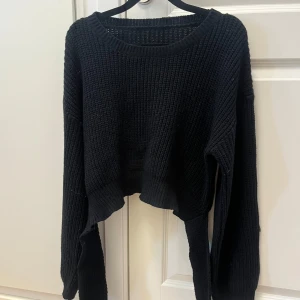 Svart croppad stickad tröja med knyt - Svart stickad tröja med lång ärm och croppad passform. Baksidan har en snygg knutdetalj och en öppen rygg, vilket ger en unik look. Perfekt för dig som gillar trendiga och bekväma plagg med lite edge.
