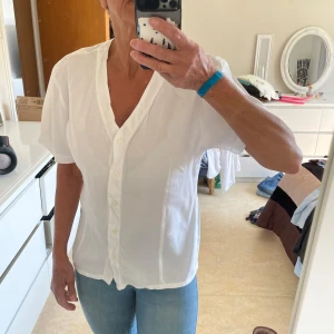 Vit kortärmad skjorta No 1 Collection - Vit skjorta från No 1 Collection i 100% viskos. Modellen har korta ärmar, v-ringning och knappar framtill. Skjortan är enkel och stilren med en luftig känsla, perfekt till jeans eller kjol. Storlek 38.