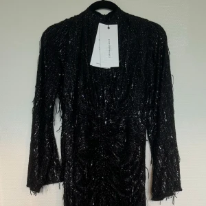 Svart lång klänning från Copenhagen Muse - Långärmad, lång exklusiv klänning med glitter/paljettdetaljer. Sitter som en smäck med vackra utsvängda ärmar och stilren lite högre krage. Köpt som julklapp, endast testad! Blev aldrig av att lämna tillbaka den i butik därav säljes här. Köpt i butik för 2300. Mitt pris 1200. Kommer med alla taggar och inslagsförpackningen från butik.