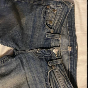 True Religion lågmidjade bootcut jeans - Säljer ett par blå jeans från True Religion med låg midja och bootcut-ben. Jeansen har klassiska true relgion märket på bakfickorna. 