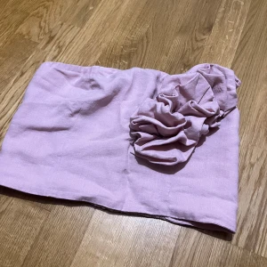 Ljuslila ofshoulder tubtopp med volang - Superfin ljuslila tubtopp med oneshoulder och stor volangdetalj över axeln. Perfekt för dig som vill sticka ut med en unik och trendig topp. Tunt och svalt tyg som passar bra till varmare dagar.