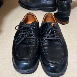 Svarta skinnskor från Black Woods - Klassiska svarta skinnskor från Black Woods med snörning och rund tå. Skorna har en stilren design med lätt texturerad ovandel och platt sula. Perfekta för dig som gillar en tidlös och clean look till vardags eller mer dressade tillfällen.