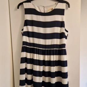 Randig klänning från Holly & Whyte - Snygg ärmlös klänning med breda marinblå och vita ränder från Holly & Whyte by Lindex. Modellen är midjekjolad med lätt rynk och har en rund halsringning samt knappdetalj i nacken. 