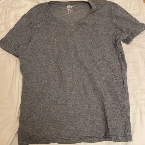 Grå basic t-shirt från H&M - Enkel och stilren grå t-shirt från H&M i mjuk bomull med stretch. T-shirten har v-ringning och korta ärmar, perfekt för en avslappnad look. Passformen är normal och materialet känns skönt mot huden.
