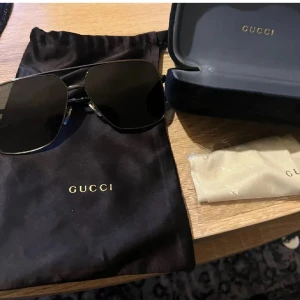 Svarta solglasögon från Gucci - Snygga svarta solglasögon från Gucci med fyrkantiga linser och tunn metallbåge. Klassisk design med diskret Gucci-logga på linsen och detaljer i silver. Kommer med originalfodral, putsduk och påse. Ny pris 5400