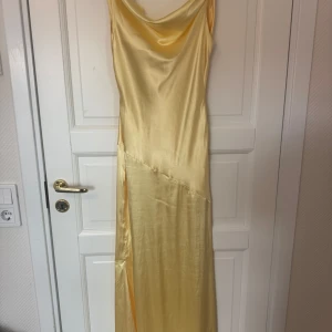 Ljusgul långklänning i satin - Snygg ljusgul långklänning i satin med draperad urringning och smala axelband som korsas i ryggen. En perfekt klänning som passar till många tillfällen. Jag är 170 och den går ner till fötterna på mig. Är både en 34 och 36. Priset går att diskutera