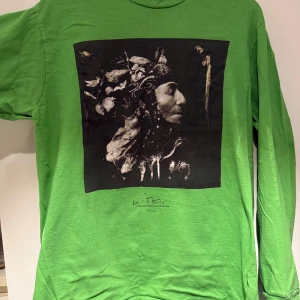 Grön långärmad Supreme-tröja M - Supreme långärmad tröja i grön bomull med svartvit konstgrafik på bröstet. Klassisk crewneck och Supreme-logga i nacken. Perfekt statement-piece för dig som gillar streetwear och unika prints.