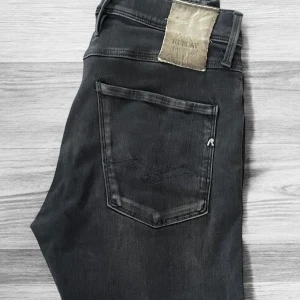 Replay Anbass Hyperflex svarta jeans - Hej, säljer nu ett par svarta Replay Anbass Hyperflex jeans. Jeansen har raka ben och normal passform, tillverkade i stretchigt jeanstyg för extra komfort. Snygg Replay-logga på bakfickan och läderpatch i midjan. De har inga som helst defekter utan bara ett litet hål vid gylfen som är översytt med svart i samma färg som byxan och bara använda. Storlek 31✅ Hör av dig vid minsta fundering, pris går att diskutera😊