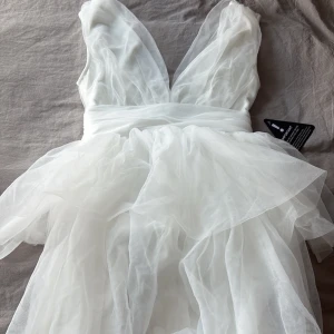 Vit tyllklänning med v-ringning - Supersöt vit tyllklänning i kort modell med djup v-ringning och omlottkänsla upptill. Klänningen har flera lager tyll som ger en fluffig och drömmig look. Prislappen kvar! 💘💘