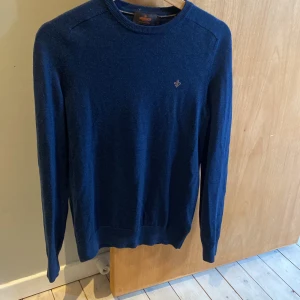 Marinblå merinoulltröja Morris S - Snygg marinblå stickad tröja från Morris i 100% merinoull. Klassisk rund halsringning och diskret logga broderad på bröstet. Perfekt för dig som gillar stilrena och bekväma plagg med premiumkänsla.
