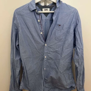 Blå skjorta från Tommy Jeans - Snygg blå skjorta från Tommy Jeans med klassisk krage, bröstficka och vita knappar. Skjortan har lång ärm och är tillverkad i mjuk bomull. Perfekt för en avslappnad men stilren look.