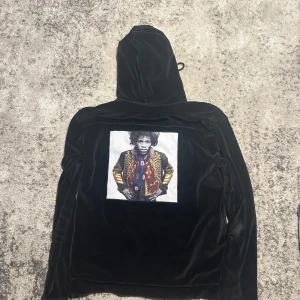 Limitato zip hoodie - Svart hoodie i mjuk velour med dragkedja framtill och två fickor med dragkedja. Stor huva med snörning och ett stort färgstarkt tryck på ryggen. Perfekt för dig som vill sticka ut med en unik look.