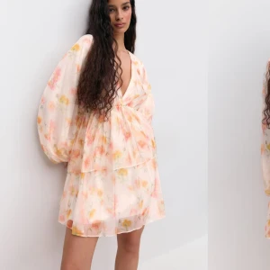 Blommig kortklänning - Supersöt kortklänning från Gina Tricot med blommigt mönster i ljusa toner av rosa, orange och gult. Klänningen har v-ringning, långa puffärmar och volangdetaljer. Tillverkad i ett tunt, flowy material som känns luftigt och somrigt. Storlek S men skulle mer säga att den sitter som en M. Endast testad annars helt oanvänd! Nypris 499kr