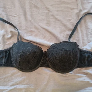 Svart bh från Kappahl - Snygg svart bh från Kappahl med broderade detaljer på kuporna. Avtagbara axelband med lätt vaddering och bygel för extra stöd. Gjord i polyamid och elastan för en skön och följsam känsla. Perfekt för att lyfta din outfit med en elegant touch.