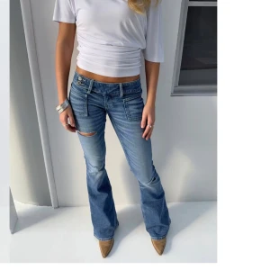 Blå bootcut jeans med slitning - Snygga blå bootcut jeans med slitning på ena benet och stora framfickor. Jeansen har låg midja och klassisk jeanslook med lätt tvättad effekt. Perfekta för en avslappnad och trendig stil. Pris kan diskuteras vid snabb affär💞