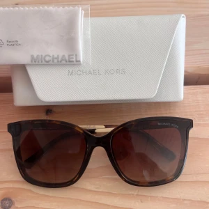Bruna solglasögon från Michael Kors - Snygga solglasögon från Michael Kors med brunmelerad båge, en liten repa i ena glaset men inget man tänker på alls (se bilder)🥰 original oöppnad putsduk och fodral medföljer, köpa för 1700🥰pris kan diskuteras vid snabb affär!! 