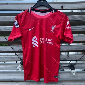🟥 Liverpool Hemmatröja 21/22 – M. Salah #11 – Herrstorlek S - Säljer en Liverpool FC hemma tröja från säsongen 2021/2022.  🔴 Spelarnamn: Mohamed Salah #11 (officiellt tryck) 🔴 Storlek: S (Small) – herrmodell 🔴 Märke: Nike Dri-Fit 🔴 Premier League-märke på ärmarna 🔴 Mycket fint skick, endast använd ett fåtal gånger. Inga fläckar eller skador.  Perfekt för dig som är Liverpool-supporter eller samlare!