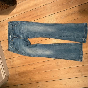 Levi's blå bootcut jeans - Säljer ett par klassiska blå Levi's jeans med bootcut passform och snygga detaljer på bakfickorna. Jeansen har normal midja och är tillverkade i mjukt denim med lätt slitning framtill. Perfekta för dig som gillar en tidlös och avslappnad stil. Oklart vilken storlek men passar XS-M