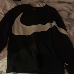 Svart Nike sweatshirt med stor logga - Svart sweatshirt från Nike i storlek S med en stor vit swoosh-logga tvärs över framsidan. Klassisk crewneck-modell med långa ärmar och broderad Nike-logga på ärmen. Mjuk och skön bomullsblandning, sitter jätteskönt. är i storlek s men funkar för xs 