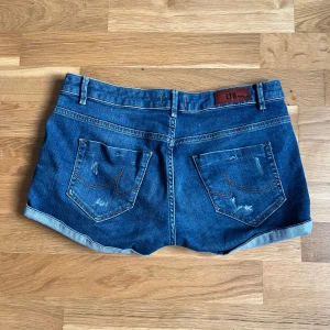 Blå jeansshorts från LTB - Snygga blå jeansshorts från LTB med uppvikta benslut och slitna detaljer på både fram- och baksida. Klassisk femficksmodell med bälteshällor och kontrastsömmar. Perfekta för en avslappnad stil under varma dagar.