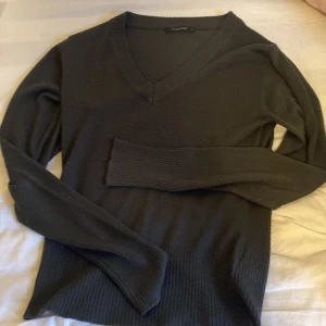 Svart v-ringad tröja från b.young - Svart v-ringad tröja från b.young i storlek S. Tröjan har långa ärmar, bred ribbad mudd vid ärmslut och nederkant samt en klassisk passform. Perfekt att styla med jeans eller kjol för en clean look.