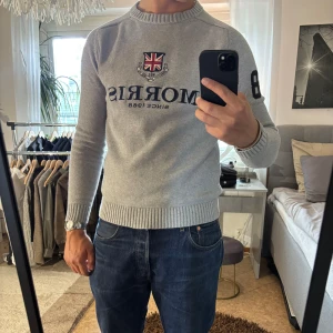 Grå stickad tröja från Morris - Snygg grå stickad tröja från Morris med broderad Union Jack-logga och text på bröstet. Tröjan har ribbade muddar, rund hals och svart siffra 8 på ena ärmen. (Notering) Jag har storlek M egentligen så den sitter lite tajt på mig. 