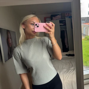 Ljusgrön ribbad blus med knyt i ryggen - Superfin ljusgrön blus med breda ribbade ränder och korta ärmar. Snygg detalj med knyt i ryggen som ger en unik look. Blusen har en lite boxig passform och hög hals, perfekt till både jeans och kjol.