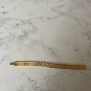 Guldigt armband från lacoste - Snyggt armband i guldton från Lacoste med breda länkar och stilren design. Ena sidan har en texturerad yta som ger extra detalj, medan andra sidan är slät och matt. Perfekt accessoar för att lyfta din outfit.