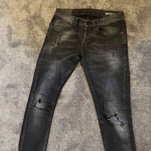 Svart/grå dondup jeans  - Svarta jeans från dondup med slitna detaljer på låren och knäna. Klassisk femficksmodell med dragkedjegylf och låg midja. Perfekta för en trendig och avslappnad stil.  Modellen är George och storleken är w31 