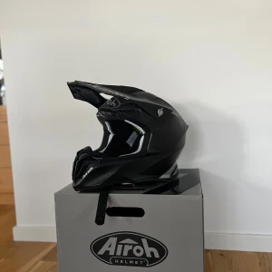 Svart crosshjälm från Airoh - Säljer en mattsvart crosshjälm från Airoh med coola vita detaljer och loggor. Hjälmen har en skärm framtill och är utrustad med svarta 100% goggles. Snygg och sportig design som passar perfekt för motocross eller enduro. Storlek: L