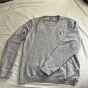 Grå sweatshirt från Morris, storlek M - Snygg grå sweatshirt från Morris i storlek M. Tröjan har rund halsringning, långa ärmar och en liten broderad logga på bröstet. Tillverkad i mjuk bomull som är skön att ha på sig. Perfekt för en clean och stilren look. Tröjan är iprincip nyskick😃