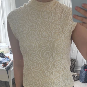 Ljusgul mönstrad ärmlös topp - Supersnygg ljusgul topp med hög hals och ärmlös design. Toppen har ett unikt, broderat mönster som ger en cool struktur och sticker ut. Perfekt för dig som gillar detaljer och vill ha något annorlunda i garderoben.