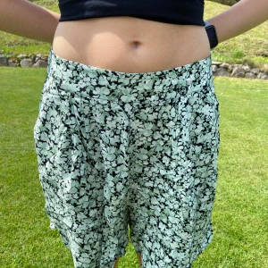 Blommiga shorts från Gina Tricot - Helt nya och oanvända men ostrukna på bilden! Snygga blommiga shorts från Gina Tricot i svart och mintgrönt. De har en lös passform och ser även ut som en kjol. Fin viskose kvalité för fint fall. Perfekta för varma dagar. Mjukt och lätt material som känns skönt mot huden.