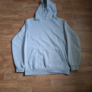Ljusgrå hoodie från SMOG - En enkel och stilren ljusgrå hoodie från SMOG i storlek M. Tröjan har en klassisk huva, magficka och ribbade muddar vid ärmslut och nederkant. Perfekt för en avslappnad look. Jag har själv klippt av snörrerna på luvan.