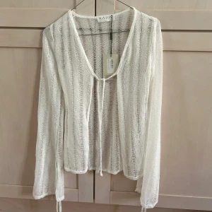 Vit transparent stickad blus/kofta från Kaiia - Säljer en vit, transparent och lätt stickad blus/kofta från Kaiia. Blusen har långa ärmar, v-ringning och knyt framtill. Även Snygg detalj med knytband vid ärmslut.