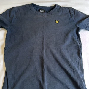 Mörkblå t-shirt från Lyle & Scott - Säljer en mörkblå t-shirt från Lyle & Scott med klassisk gul broderad logga på bröstet. T-shirten har rund halsringning och är tillverkad i mjuk bomull. Perfekt för en stilren och enkel look.
