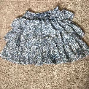 Blå volangkjol med vitt leopardmönster - Säljer en blå kortkjol med flera volanger och vitt leopardmönster. Kjolen har resår i midjan och är luftig och lätt, perfekt för varma dagar. Mönstret ger en cool och trendig look. skriv för fler bilder🥰