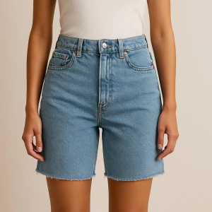 Blå jeansshorts från Never Denim - Säljer ett par klassiska blå jeansshorts från Never Denim med hög midja och råa, fransade benslut. Shortsen har fem fickor och stängs med knapp och . Perfekta för sommaren!