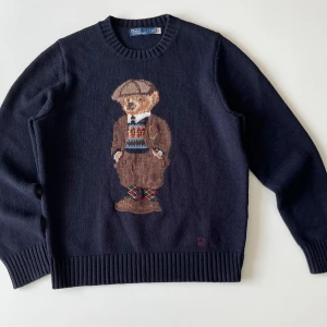 Mörkblå stickad tröja med björn från Polo Ralph Lauren - Säljer en mörkblå stickad tröja från Polo Ralph Lauren med den klassiska broderad björn på framsidan. Skick är 10/10 och har använts ändast 1 gång. Priset går att diskuteras vid snabb affär.