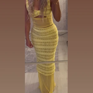 Gul två delad set med volangdetaljer - Säljer ett snyggt gult set  med volangdetaljer och cut-out vid midjan. Klänningen har ärmlös design och figurnära passform som framhäver siluetten. Perfekt för dig som vill sticka ut med en färgglad look!