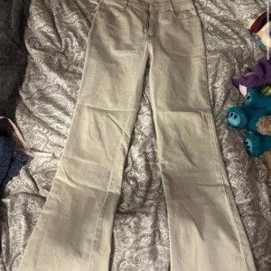 Beige/kräm vita bootcut byxor från Quine - Snygga beige byxor från Quine med bootcut passform. Byxorna har broderad detalj på bakfickan och dekorativa sömmar vid fickorna fram. Nypris 1000kr. Knappen har åkt av en gång tidigare men sitter på nu, därför de låga priset .  Oanvända 
