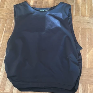 Svart ärmlös topp från SHEIN - Säljer en svart ärmlös topp från SHEIN i storlek Petite L. Toppen har en enkel design med rynkade detaljer på sidan som ger en snygg siluett. Perfekt att matcha med både jeans och kjol.