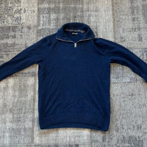 Mörkblå tröja med dragkedja från Jack & Jones - Säljer en mörkblå långärmad tröja från Jack & Jones med halv dragkedja i halsen. Tröjan har en hög krage och är tillverkad i ett mjukt material, perfekt för kyligare dagar.