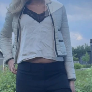 Ljusbeige quiltad jacka med dragkedja - Säljer en ljusbeige quiltad jacka med svarta detaljer och dragkedja framtill. Jackan har lång ärm och två fickor med knappstängning. Perfekt för kyligare dagar och enkel att matcha till olika outfits. Storlek S men passar även M