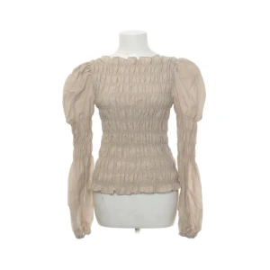 Beige blus med puffärmar och smock - Trendig beige blus med smock över hela kroppen och långa puffärmar. Blusen har en rak halsringning och är tillverkad i ett lätt, vävt material som ger en luftig känsla.